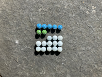 Colourful marbles arranged on a five by five grid. The first row is filled with blue marbles. There are two green marbles in the second row. In the third row the first two columns are empty, the remaining columns are occupied by white marbles. The fourth and fifth rows are filled with white marbles.