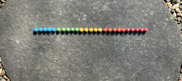 Colourful marbles, arranged in a row of twenty five.